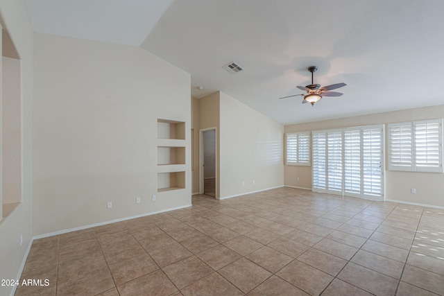 spare room featuring lofted ceiling, built in shelves, plenty of natural light, and tile patterned floors