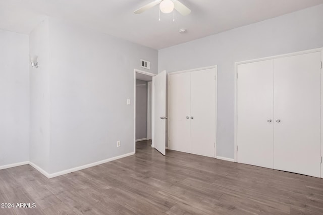 unfurnished bedroom with hardwood / wood-style flooring, ceiling fan, and multiple closets