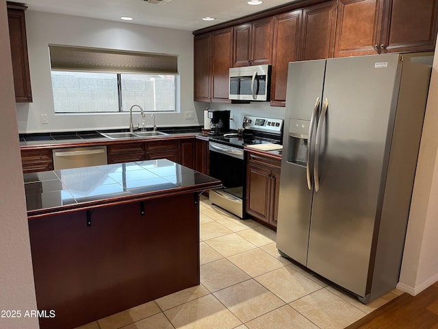 kitchen with light tile patterned flooring, sink, dark brown cabinets, appliances with stainless steel finishes, and tile counters