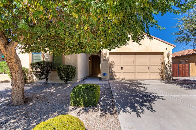 view of property hidden behind natural elements featuring a garage, concrete driveway, fence, and stucco siding