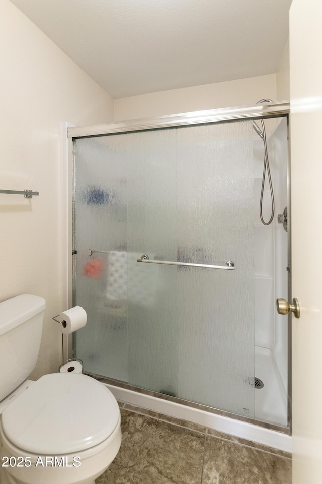 bathroom featuring a shower with door and toilet