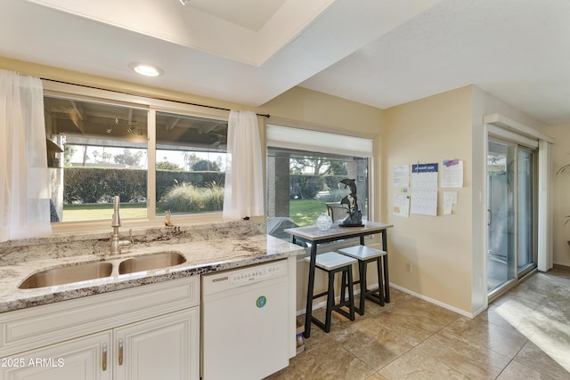 kitchen featuring white dishwasher, sink, light stone counters, and white cabinets