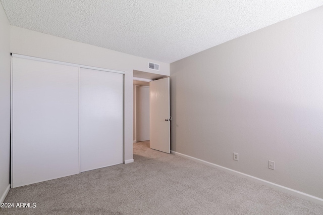 unfurnished bedroom with light carpet, a textured ceiling, and a closet