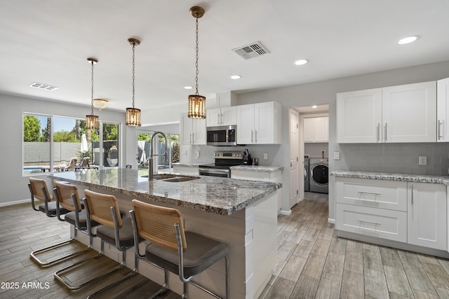 4904 E Tierra Buena Ln, Scottsdale, AZ 85254 - kitchen with visible vents, washer / clothes dryer, a sink, appliances with stainless steel finishes, and wood finish floors