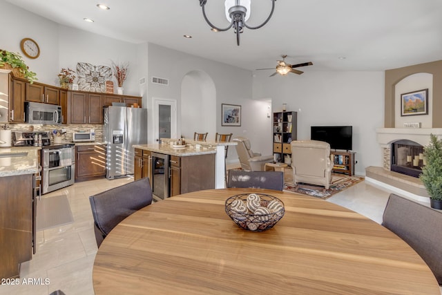 tiled dining space with ceiling fan, beverage cooler, and a high ceiling