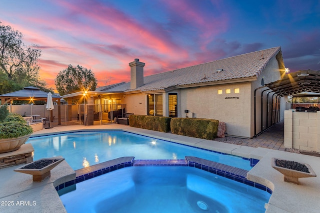 pool at dusk featuring a gazebo, a patio area, and an in ground hot tub