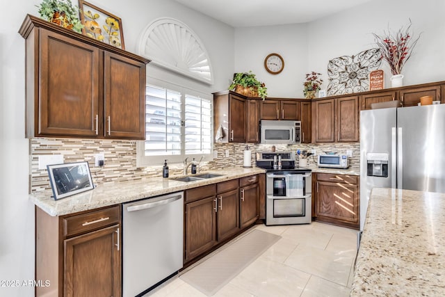 kitchen featuring sink, light stone counters, light tile patterned floors, stainless steel appliances, and decorative backsplash