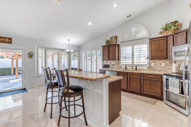 kitchen with lofted ceiling, light stone counters, a center island, pendant lighting, and stainless steel appliances