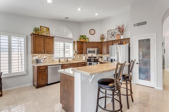 kitchen featuring a breakfast bar area, appliances with stainless steel finishes, a kitchen island, light stone countertops, and decorative backsplash