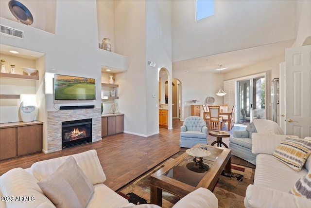 living room with dark hardwood / wood-style floors, a stone fireplace, a towering ceiling, and built in shelves