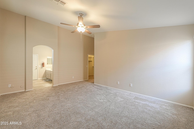 unfurnished bedroom with arched walkways, light colored carpet, visible vents, ensuite bathroom, and high vaulted ceiling