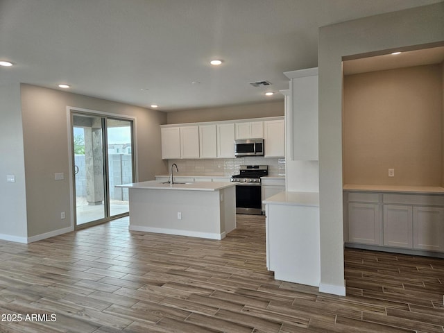 3390 S 180th Ln, Goodyear, AZ 85338 - kitchen featuring appliances with stainless steel finishes, wood finished floors, tasteful backsplash, light countertops, and a center island with sink
