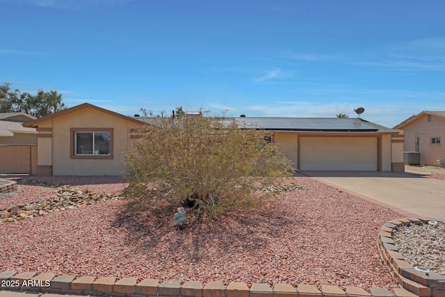 ranch-style home featuring cooling unit, an attached garage, stucco siding, concrete driveway, and roof mounted solar panels