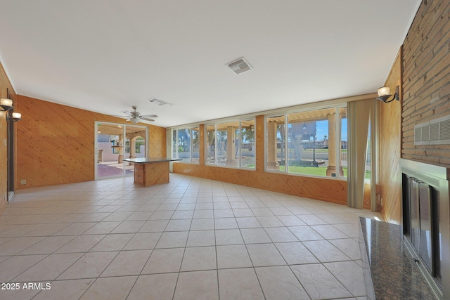 unfurnished living room featuring light tile patterned floors, visible vents, a large fireplace, and wood walls