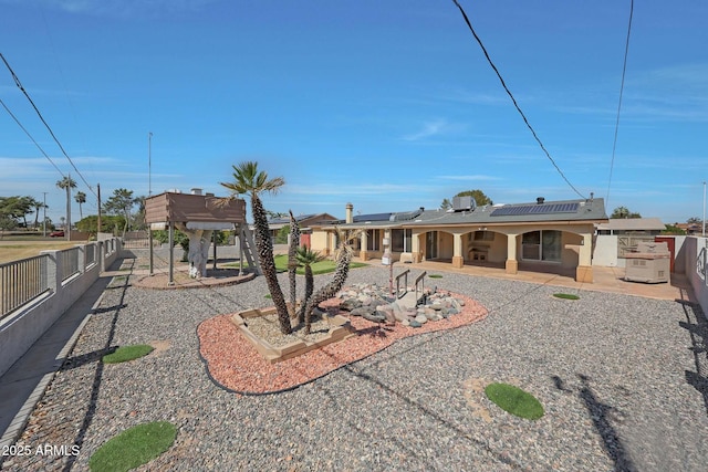 rear view of house with stucco siding, a patio, solar panels, and fence