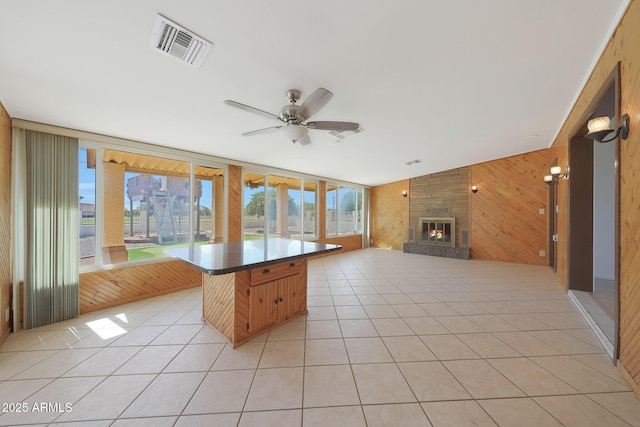 interior space featuring visible vents, open floor plan, light tile patterned flooring, wood walls, and a fireplace