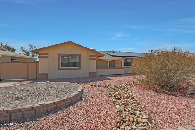 back of house featuring stucco siding, roof mounted solar panels, and fence