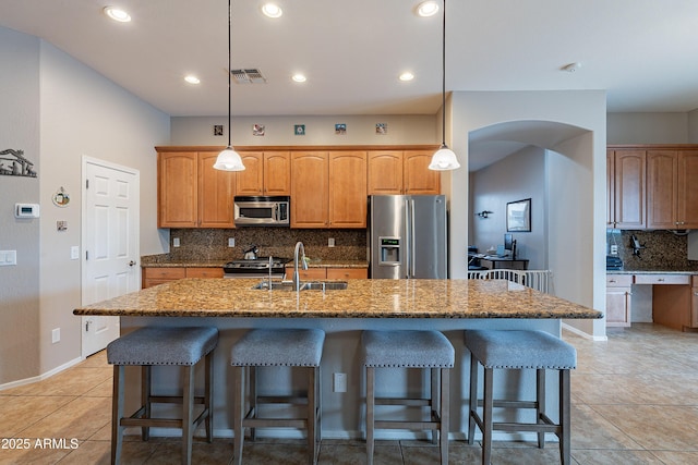 kitchen with arched walkways, a breakfast bar area, stainless steel appliances, visible vents, and a sink