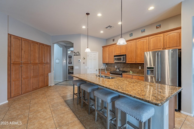 kitchen featuring arched walkways, stainless steel appliances, decorative backsplash, stone countertops, and a sink