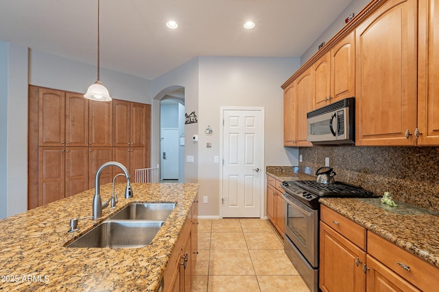 kitchen featuring light stone counters, arched walkways, stainless steel appliances, tasteful backsplash, and a sink