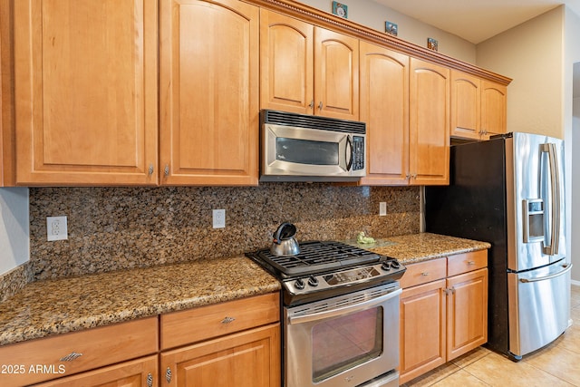 kitchen featuring appliances with stainless steel finishes, light tile patterned flooring, decorative backsplash, and light stone countertops