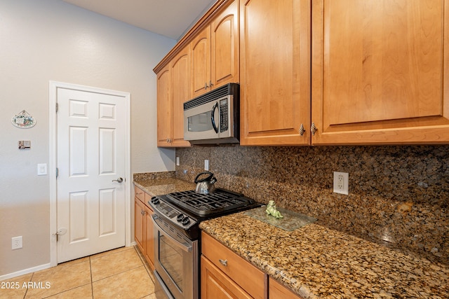 kitchen featuring light tile patterned floors, baseboards, appliances with stainless steel finishes, tasteful backsplash, and dark stone countertops