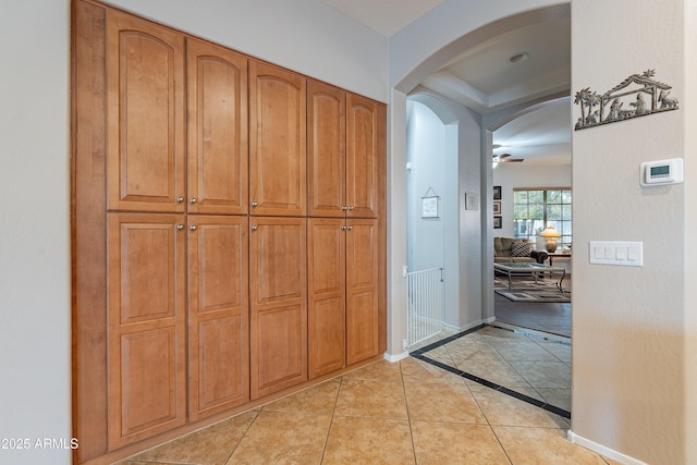 corridor featuring arched walkways, light tile patterned floors, and baseboards