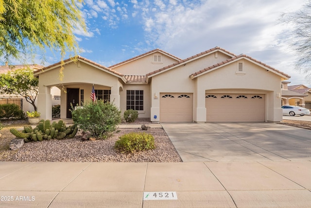 mediterranean / spanish-style home with an attached garage, a tile roof, concrete driveway, and stucco siding