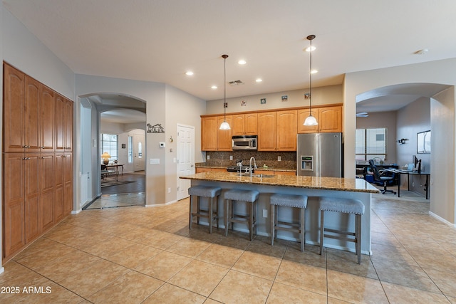 kitchen with stainless steel appliances, arched walkways, backsplash, and a kitchen breakfast bar