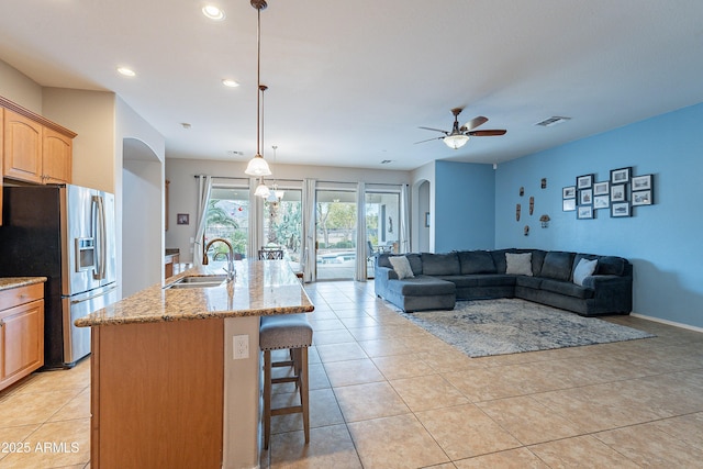 kitchen featuring light stone counters, arched walkways, a sink, stainless steel fridge, and a kitchen bar