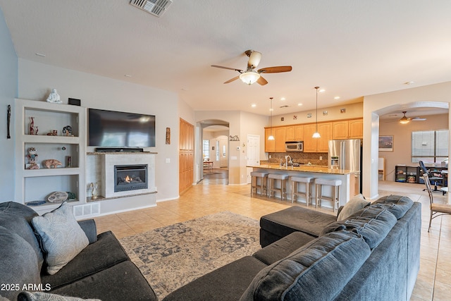 living room with a ceiling fan, arched walkways, visible vents, and a fireplace