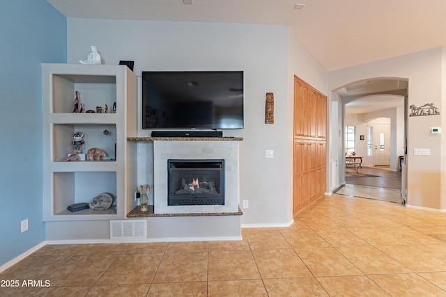 unfurnished living room with light tile patterned floors, baseboards, visible vents, arched walkways, and built in shelves