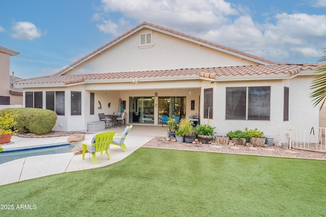 rear view of house featuring a patio, a yard, a tiled roof, and stucco siding