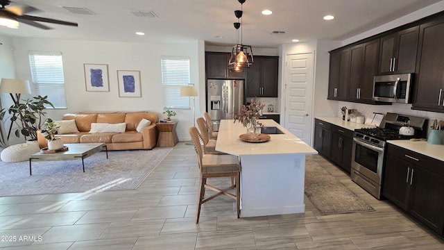 kitchen with a kitchen island with sink, hanging light fixtures, stainless steel appliances, tasteful backsplash, and a kitchen bar