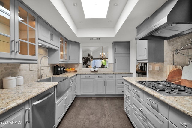 kitchen featuring sink, gray cabinetry, a tray ceiling, stainless steel appliances, and wall chimney range hood