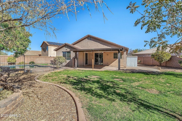 back of property with a lawn, a fenced in pool, solar panels, and a patio