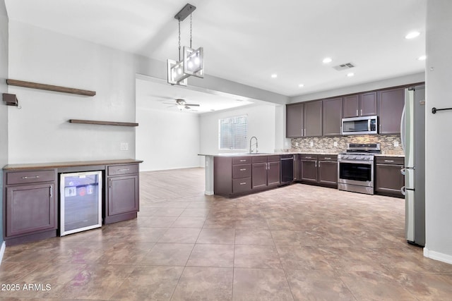 kitchen with decorative light fixtures, kitchen peninsula, sink, appliances with stainless steel finishes, and beverage cooler