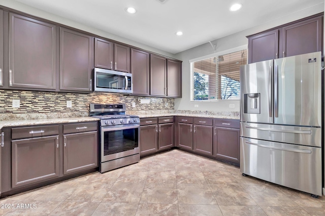 kitchen featuring dark brown cabinetry, stainless steel appliances, backsplash, light stone counters, and light tile patterned floors