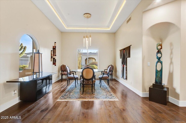 dining space with dark wood-type flooring, a raised ceiling, and a high ceiling