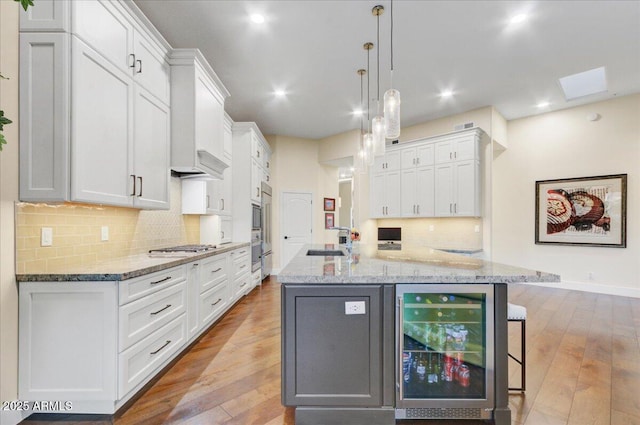 kitchen with pendant lighting, an island with sink, sink, white cabinets, and beverage cooler