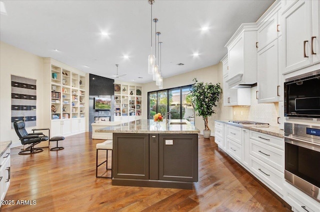 kitchen with a breakfast bar area, white cabinetry, decorative light fixtures, hardwood / wood-style flooring, and a kitchen island with sink