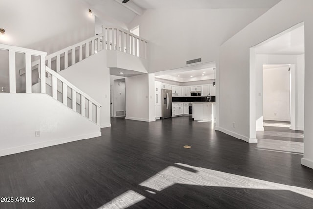 unfurnished living room with beam ceiling, high vaulted ceiling, and dark wood-type flooring