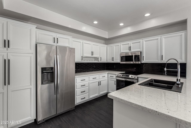 kitchen with light stone countertops, appliances with stainless steel finishes, backsplash, sink, and white cabinets