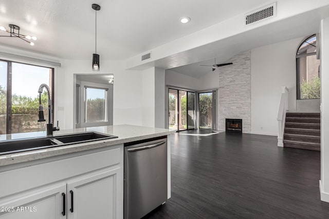 kitchen featuring a stone fireplace, sink, stainless steel dishwasher, decorative light fixtures, and white cabinetry