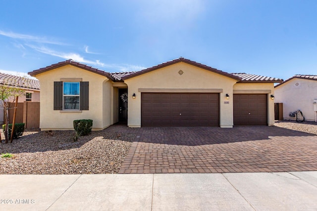 mediterranean / spanish-style home with stucco siding, an attached garage, a tile roof, and decorative driveway