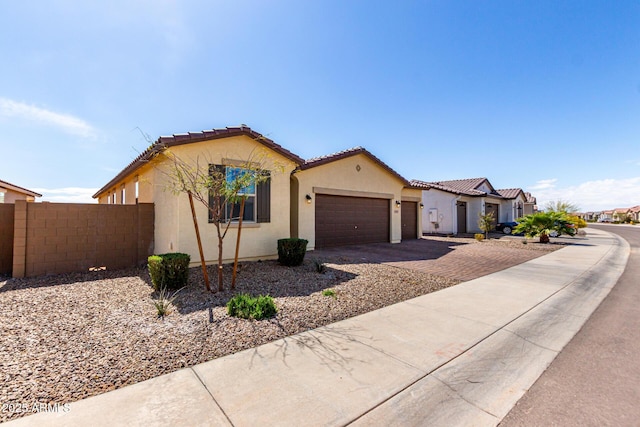 mediterranean / spanish-style home featuring an attached garage, fence, a tile roof, stucco siding, and driveway