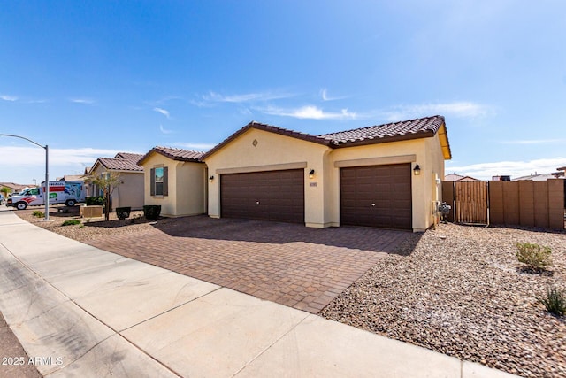 mediterranean / spanish home with a gate, an attached garage, stucco siding, a tile roof, and decorative driveway
