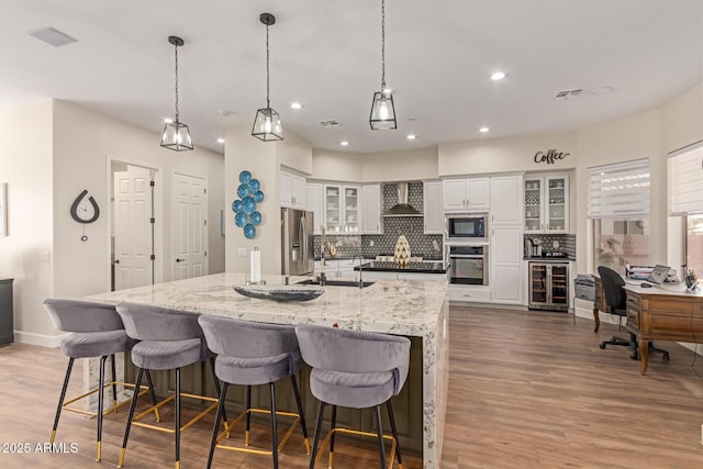 kitchen featuring a spacious island, black appliances, white cabinets, beverage cooler, and wall chimney exhaust hood