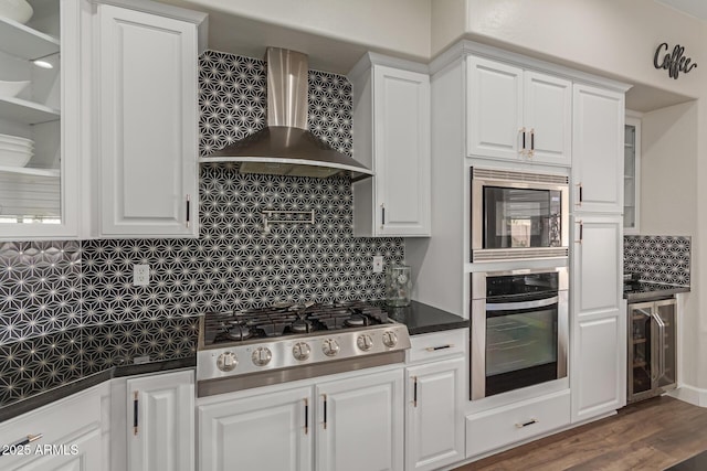 kitchen featuring wall chimney range hood, stainless steel appliances, tasteful backsplash, white cabinets, and beverage cooler