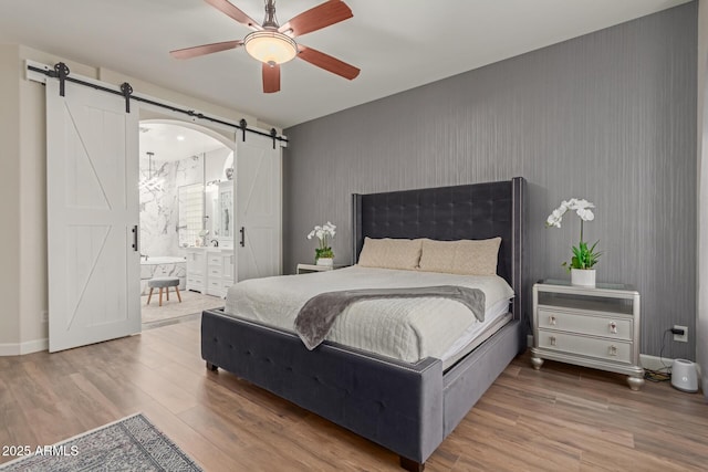 bedroom featuring ceiling fan, ensuite bathroom, a barn door, and wood-type flooring